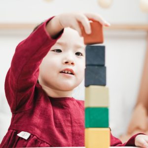 A photo of a child building coloured brick into a tower.