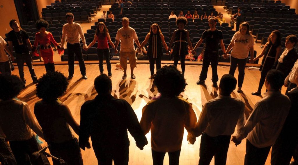 A silhouette of people holding hands in a circle in a drama studio