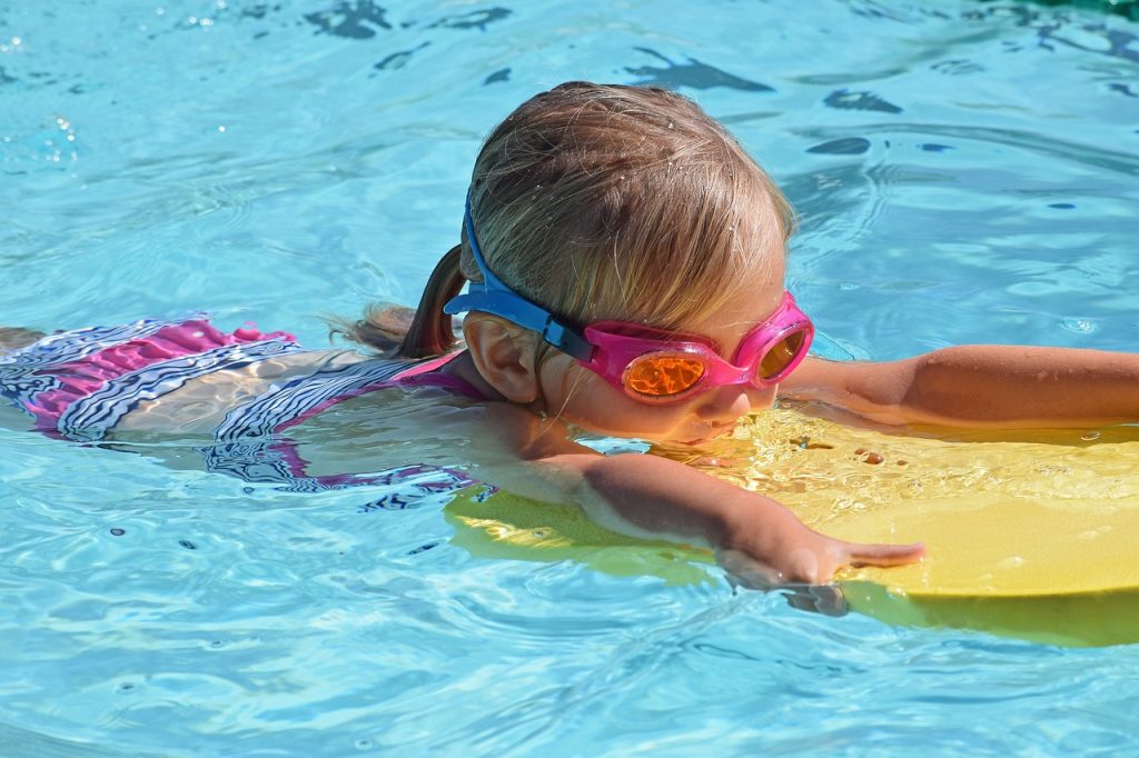 Image of a young girl swimming holding a float and wearing goggles.